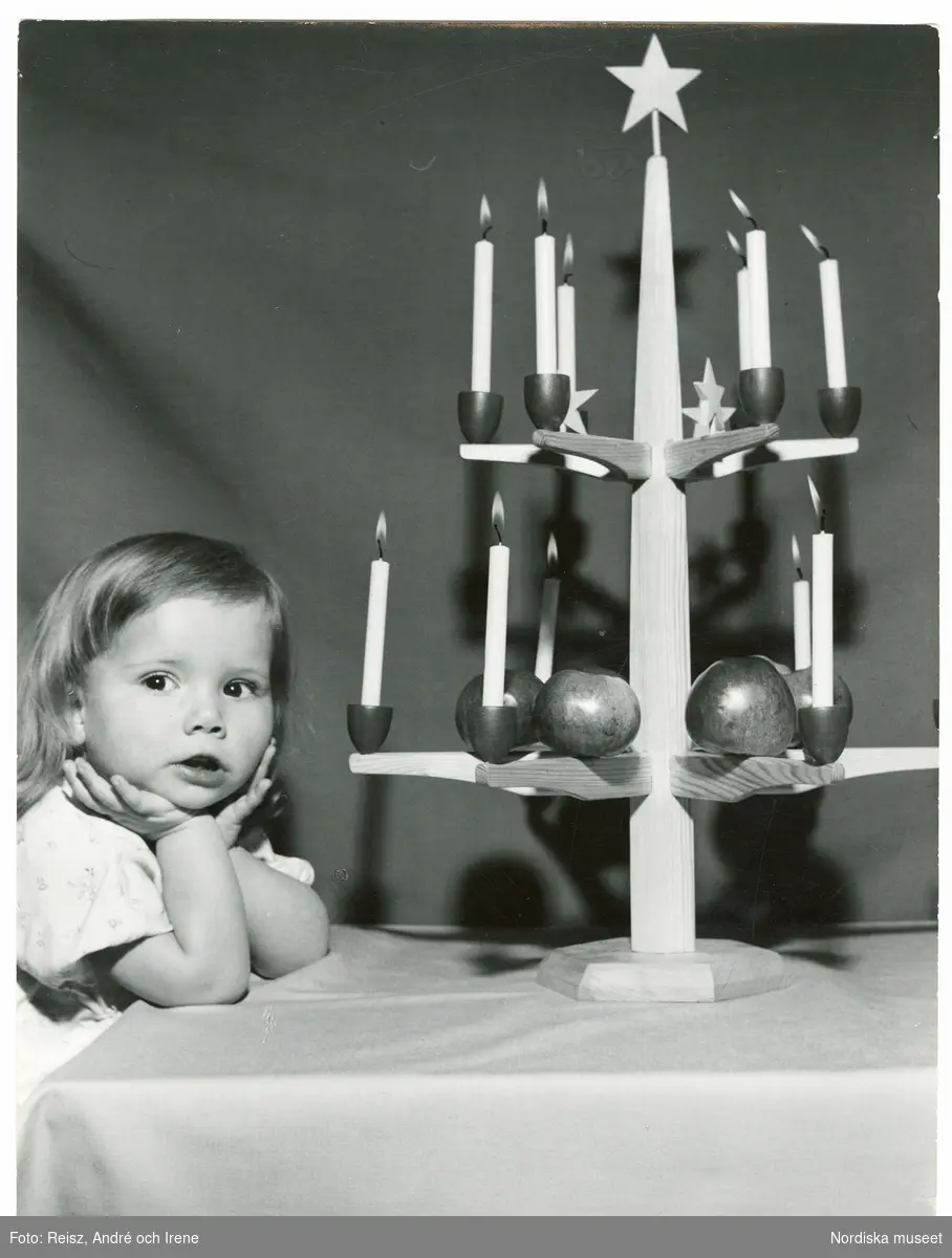 Jul. Porträtt av en flicka vid bordet med en ljusstake i trä, pyntad med färska äpplen.