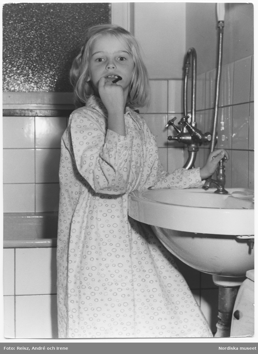 En flicka i nattlinne står vid tvättfatet i badrummet och borstar tänderna.