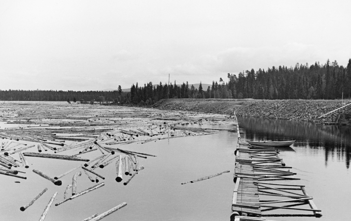 Fra innløpet til Osdammen i Valmen, der elva Søndre Osa renner ut av Osensjøen i Åmot i Hedmark.  Fotografiet er tatt i 1940.  Vi ser et stilleflytende vannspeil med fløtingstømmer.  Tømmerets gang begrenses på den ene sida, til høyre i dette fotografiet, av en jord- og grusvoll langs strandlinja.  Derfra hadde fløterne lagt ei lense, som nærmest land besto av en kjede av enkle tømmerstokker.  I den midtre delen av vassdraget lå det flåteganger, som fløterne kunne bruke som arbeidsplattformer.  Da dette fotografiet ble tatt var det ingen aktivitet på flåtegangene.  Det var imidlertid fortøyd en robåt til det beskrevne stengselet.  Den sesongen da dette fotografiet var det innmeldt 366 910 tømmerstokker til fløting ovenfor Osdammen.  Det dreide seg om virke som ble levert ved elvene Nordre Osa, Ena og Ulvsjøvassdraget, Tverrenga og ikke minst langs Osensjøens bredder.  Tømmeret ble slept i ringbommer til Valmen.  Når Osdammen ble åpnet, skapte avløpet et "sug" som med litt bistand fra fløterne og deres haker trakk stokkene mot dammens tømmerløp.