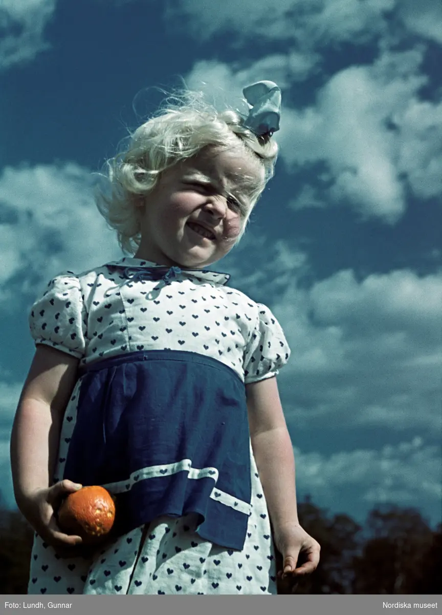 Flicka i vit klänning med hjärtmönster håller i ett äpple