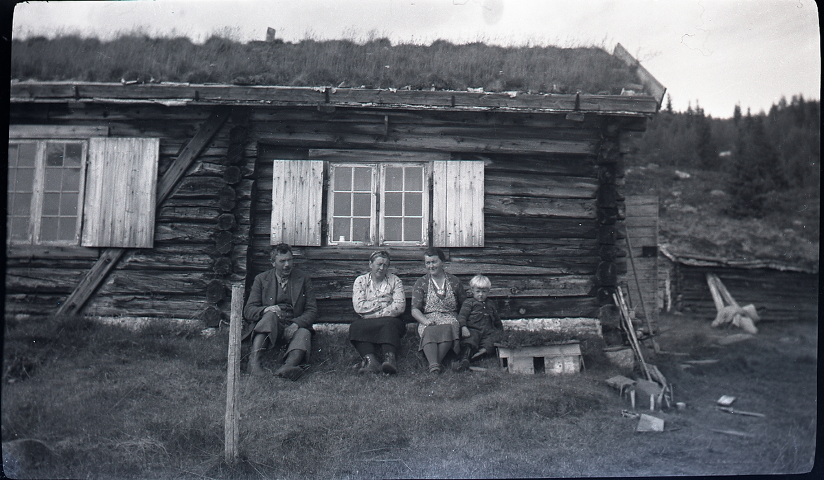Tømmerhytte på Buglebjørk som Knut Langslet kjøpte av spiritisten Kjelland i 1941. Ved hytteveggen sitter f.v. Ole Moen, Guri Moen, Alma Langslet og Lars Roar Langslet.
