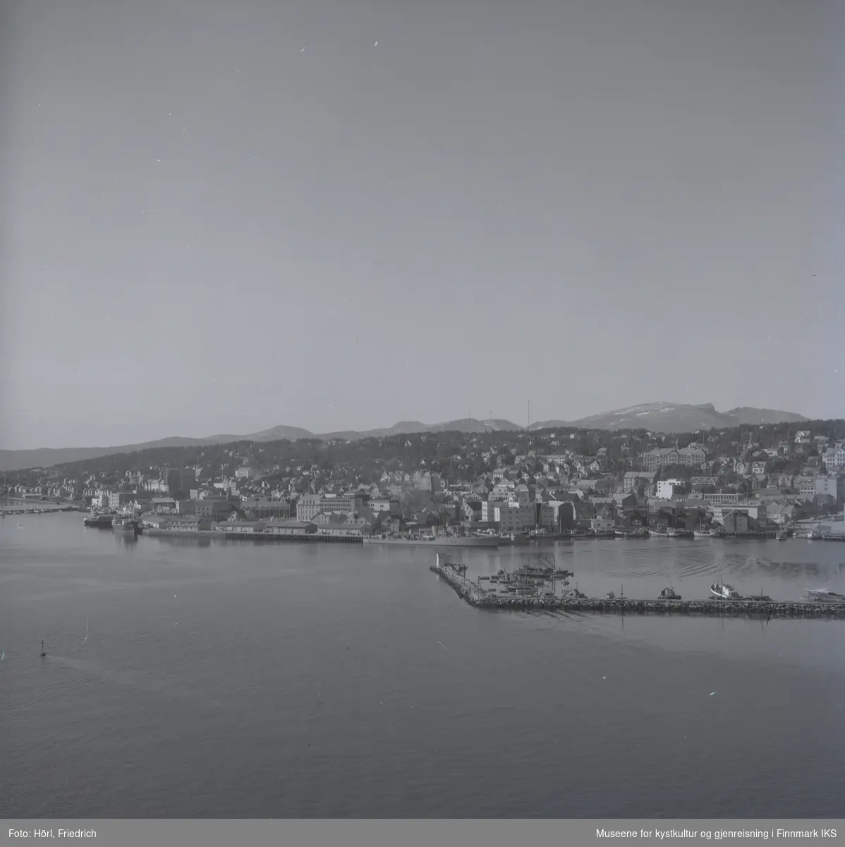 Utsikt over Tromsøs havn fotografert fra brua over Tromsøysundet. I havna ligger båter og man kan godt se bebyggelsen i byen.