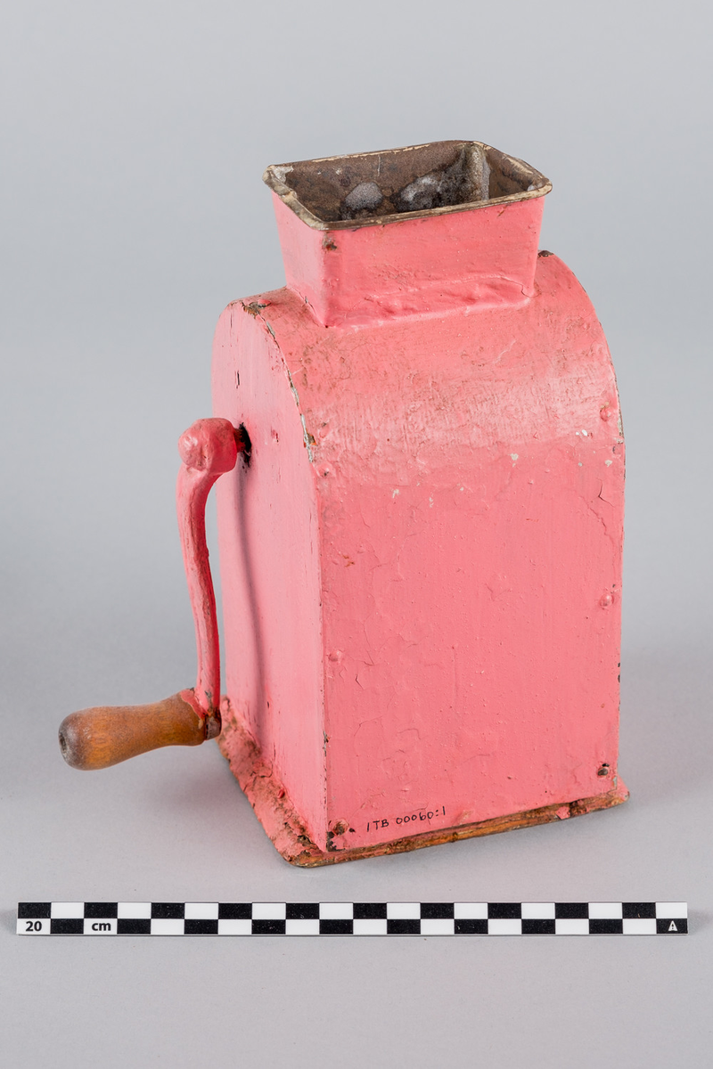 Kaffekvern i metall og tre med sveiv på siden. Buet form. Håndmalt i rosa farge. Bakre del av bunn mangler.
DELER: 1. Kvern
              2. Skuff