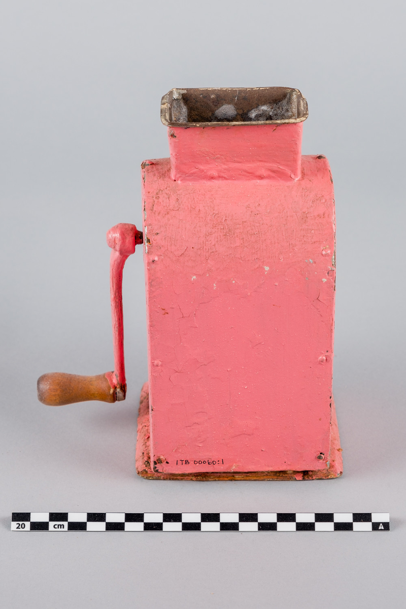 Kaffekvern i metall og tre med sveiv på siden. Buet form. Håndmalt i rosa farge. Bakre del av bunn mangler.
DELER: 1. Kvern
              2. Skuff