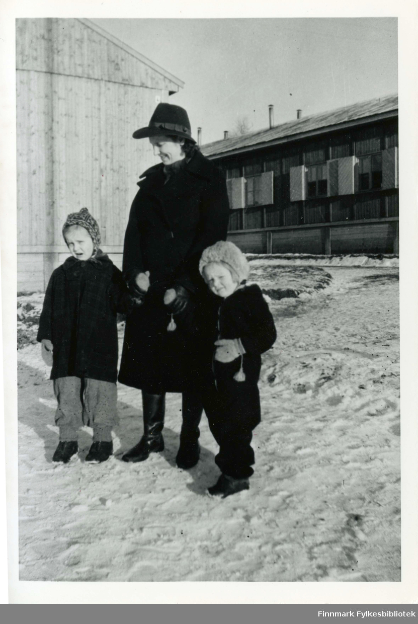6 år gammel Eli Alexandersen i 1944 med sin mor Pernille Marie og søster Berit. Eli har fortsatt med mønsterstrikket lue. Bildet er tatt i Havnås, Trøgstad. Der havnet Eli og søsteren med familie under evakuering. Mor er elegant i kåpe med hatt med «røyserta» (gummistøvler). Eli var misunnelig på søsteren som hadde dusk i vottene.
