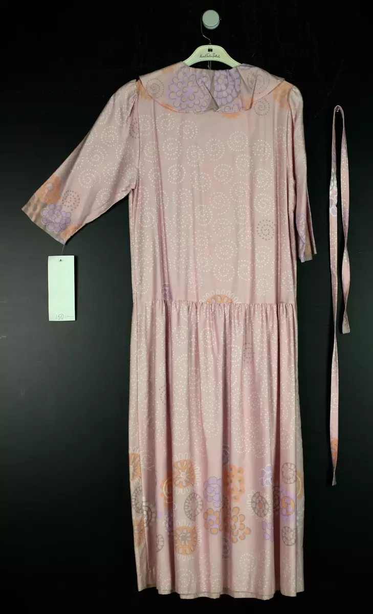 Ljusrosa klännig i textilmönstret Korall. Stor bluskrage, lågt sittande midja, klockad kjol samt tillhörande skärp.