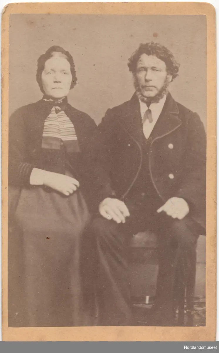 Portrett av et eldre par. Marie og Nils Grønbech. Paret sitter på stoler. Bildet er tatt utendørs foran et lerret.