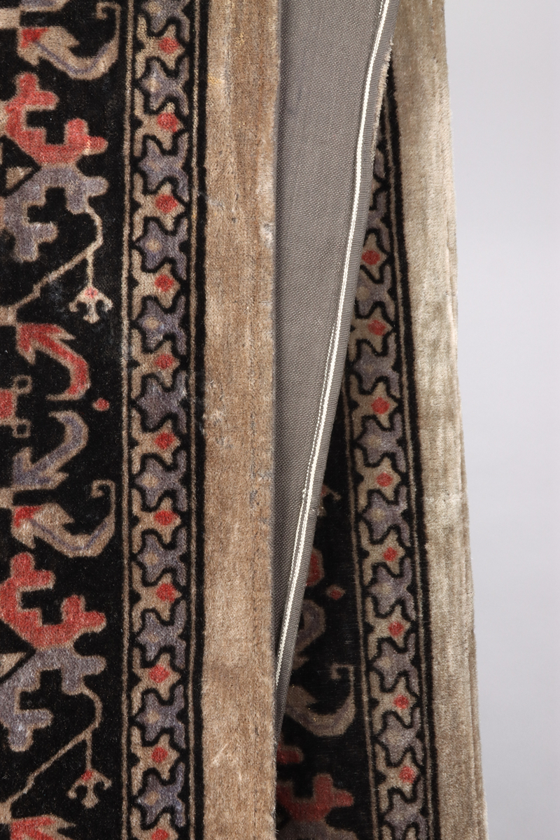 Ett överkast av mönstrad schagg. Orientaliserande mönster i färgerna grå, svart och vinröd. Del i en grupp med överkast och kuddar till en sk. Ottoman, en typ av bäddsoffa.