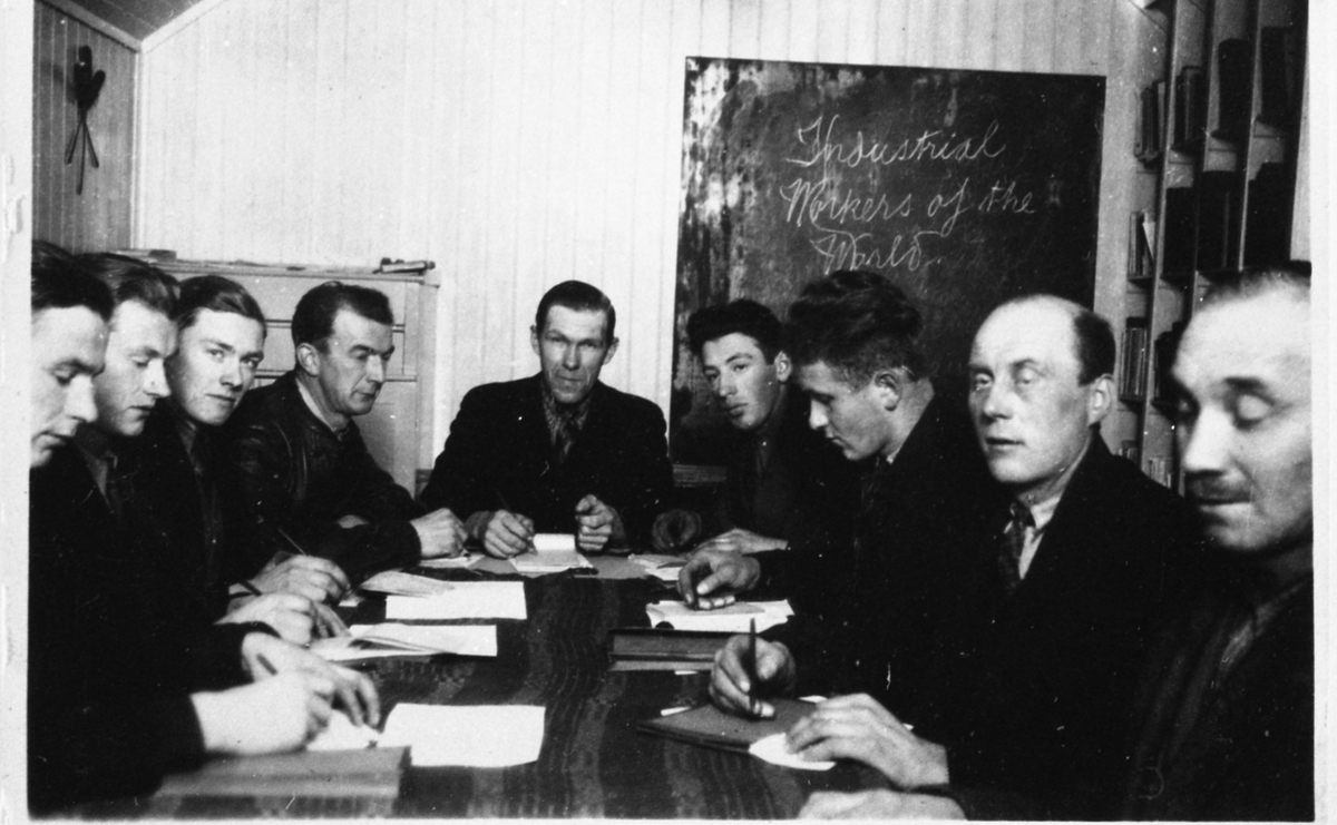 Nio män sitter samlade runt ett bord för studiecirkeln "Industrial Workers of the World", okänt plats och årtal (samma lokal och personer som A0405).
Från vänster: 1. Okänd. 2. Okänd. 3. Okänd. 4. Okänd. 5. Okänd. 6. Nils Winkvist (1911 - 1986). 7. Okänd. 8. Okänd.