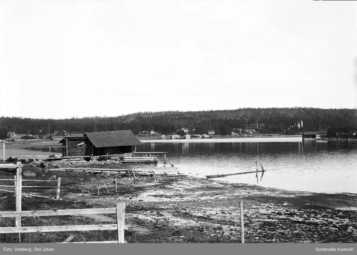 Vy över vattnet vid Bodviken. En sjöbod med tillhörande välfylld vedbod, till höger ön Lillrukan och på andra sidan vattnet till höger syns Juniskärs herrgård, senare pensionat.