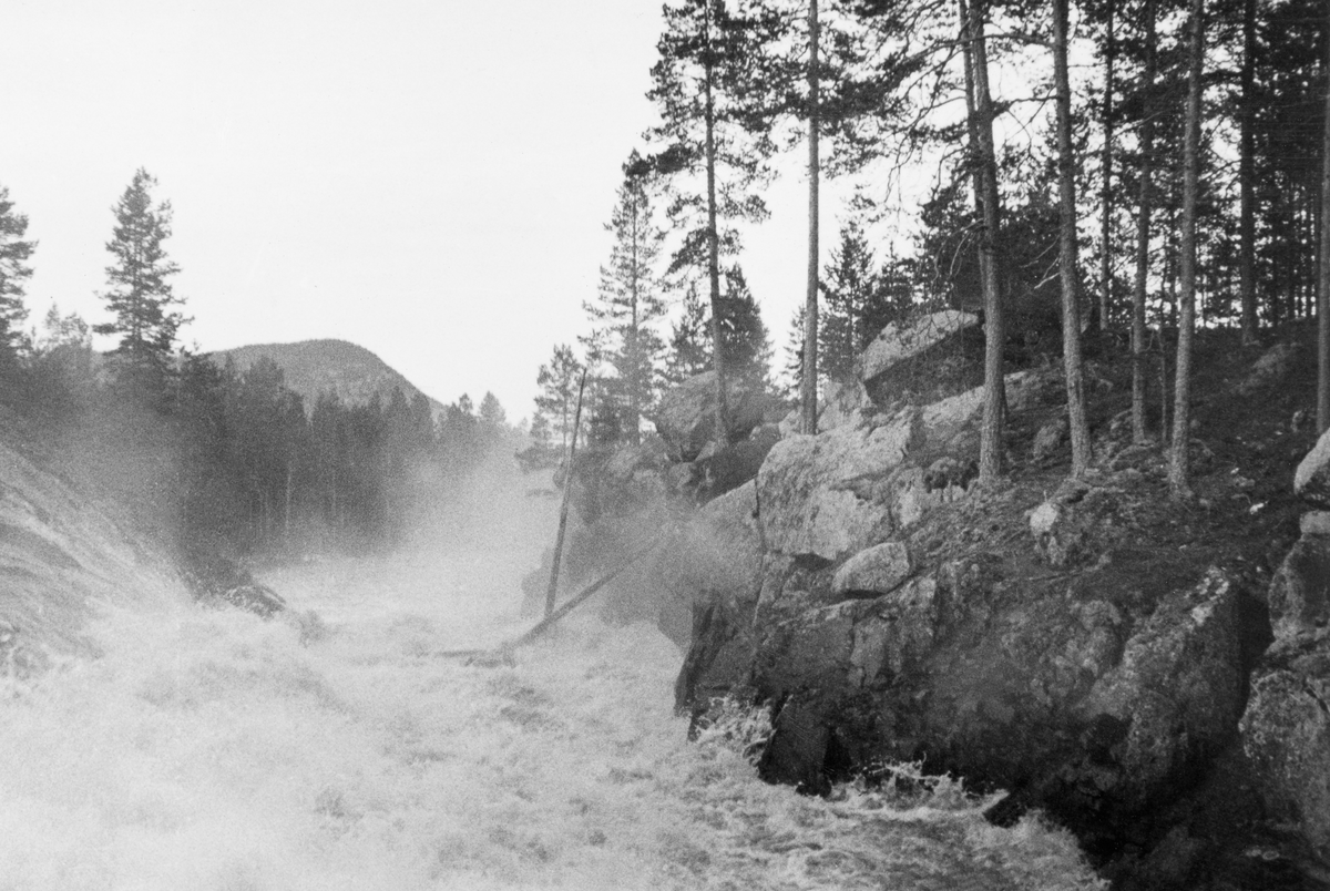 Fra Halkvernstupet, der Ytre Halåa forlater Halsjøen i Våler i Hedmark og renner gjennom ei 80-90 meter lang bergkløft med et fall på 9 meter. Fotografiet er tatt i andre halvdel av mai 1934, altså i en periode da det var rikelig med vann og betydelig fløtingsaktivitet i vassdraget. Bildet viser et kvitskummende strømkav der et par tømmerstokker reiste seg på høykant i den stride strømmen. Dette var en elvestrekning der tømmeret hadde hatt lett for å sette seg fast og bli påført skader. Forholdene var imidlertid noe forbedret etter at det var bygd skådammer langs den øvre delen av Halkvernstupet (jfr. SJD.1989-03069). I 1934 var det 73 795 tømmerstokker som ble levert ved Halåa og Halsjøen, og skulle gjennom dette vanskelige elvepartiet.