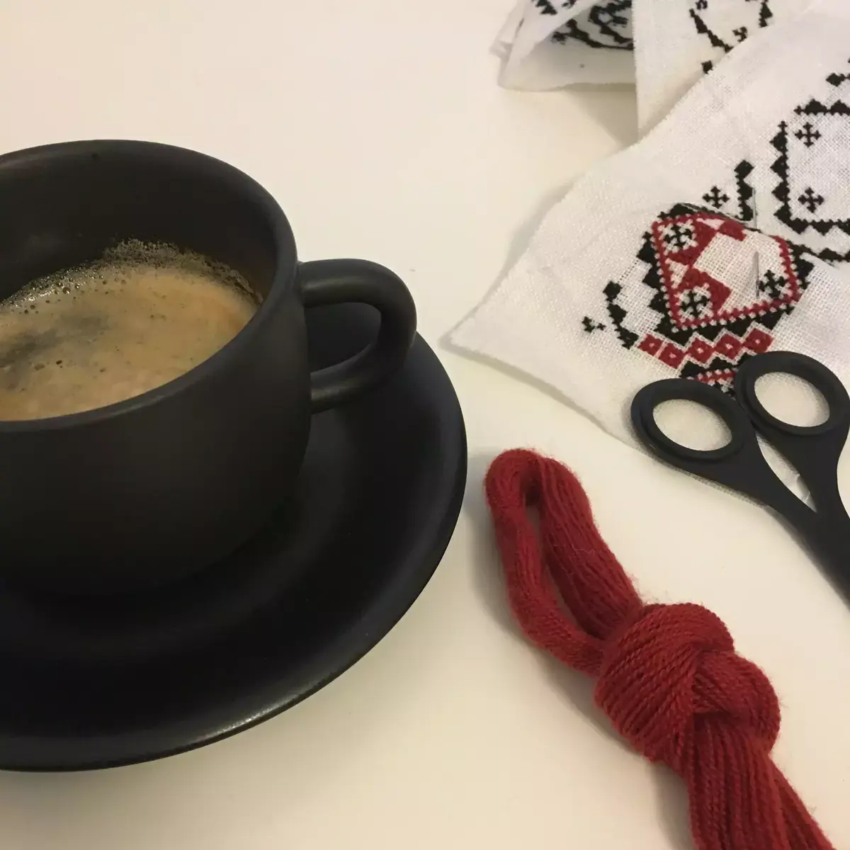 Kaffekopp med kaffe, en saks og et påbegynt broderi ligger på eit bord. 