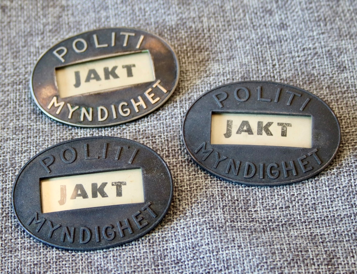 Ovalt metallmerke med teksten "Politimyndighet" og et vindu med midlertidig tekst "JAKT".
