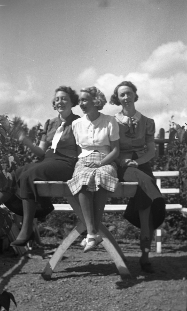 Tre kvinnor sittandes på bord, poserar framför kameran. Ingrid Sundling till vänster.