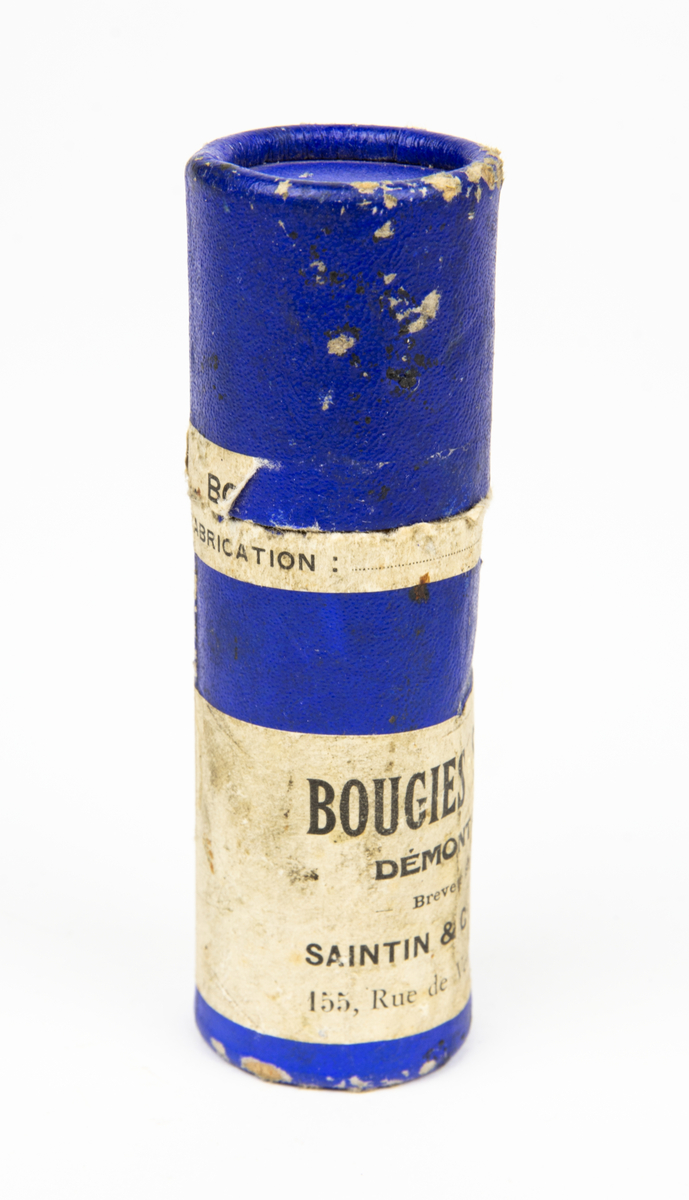 Tändstift, av fabrikat Saintin. Förvaras i originalförpackning i form av ett blått papprör med etikett med bland annat texten Bougies Saintin och dateringen 1927 Juli. I förpackningen följer en dokument. (Tändstift för motorer med hög kompression och hög hastighet.)