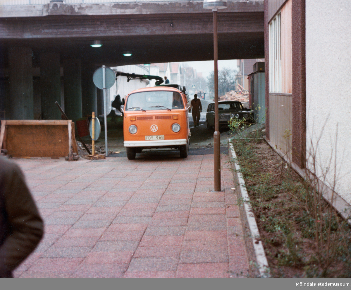 En orange folkabuss står parkerad under Mölndals Bro i Mölndals centrum, omkring 1975-1980. I bakgrunden bebyggelse på Broslätt.