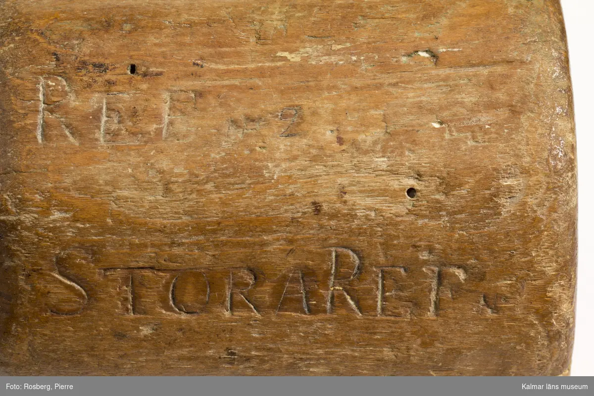 KLM 11461. Byklubba. Tillverkad av trä. Tiokantig klump med bynamnen på respektive fält. I botten text, en vers inristad av tillverkaren samt hans initialer, bomärke LR,  Min vandringstid. . . år 1800 (eller 1806).