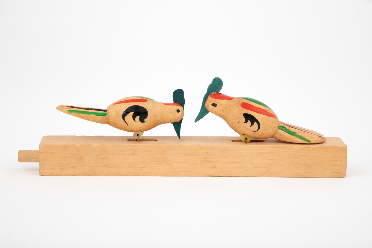 To fugler i tre montert på en stang. Fuglene er bevegelige gjennom en mekanisk styring som er montert på stangen. Fuglene er malt i rødt, grønt og svart. Svarte japanske tegn på høyre side.