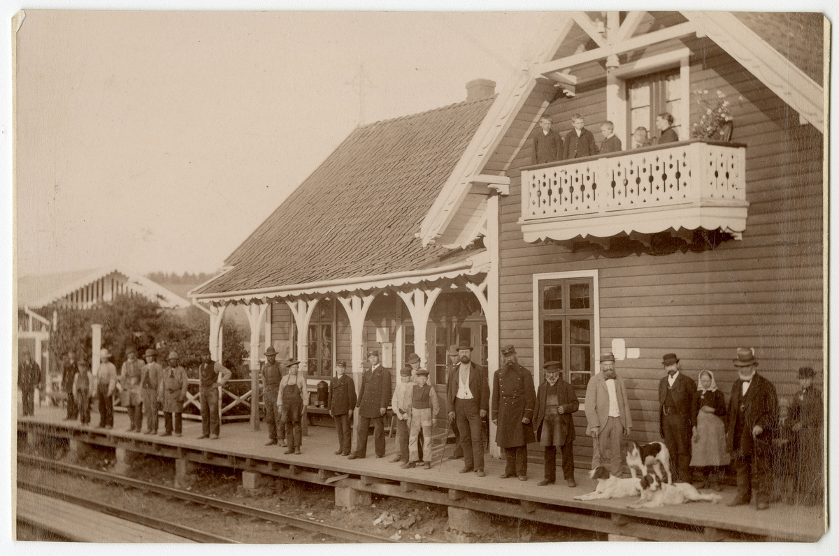 Foto av Kløfta stasjon i Ullensaker. På perrongen står flere menn i arbeidsklær og uniformer. 

Man kan se byggmester Nestor Malthe stående på høyre side av foto, ved siden av hunder (lys dress og spaserstokk)