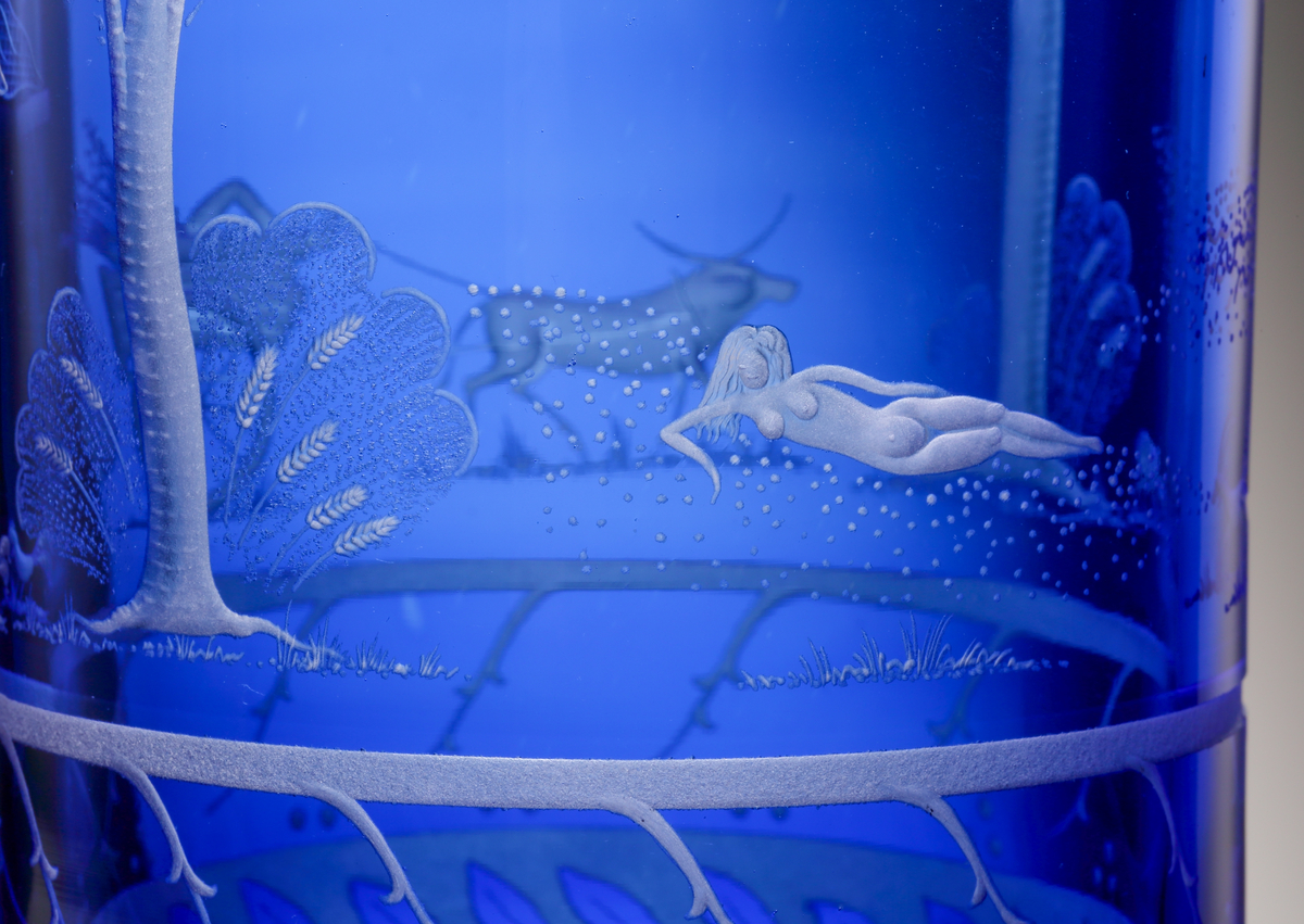 Formgivare: Gunnar Cyrén. Vas med bägarform med blå fond. På livet graverad dekor föreställande scener ur visan
"Oxdragarsång" av Evert Taube.