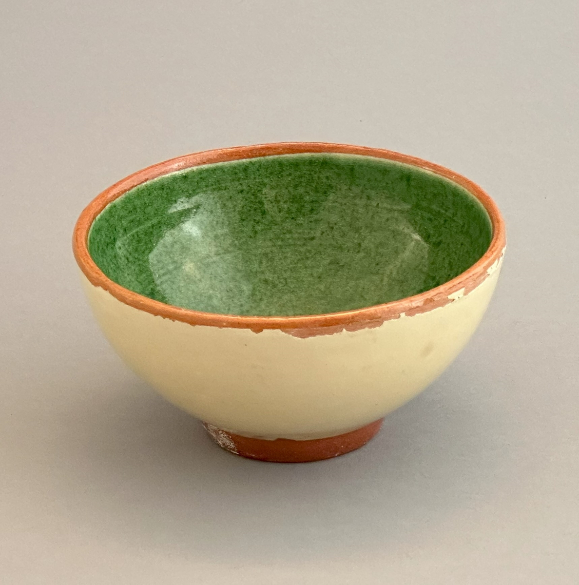 Gul skål av lergods med grön insida samt rödbrun kant och bas.