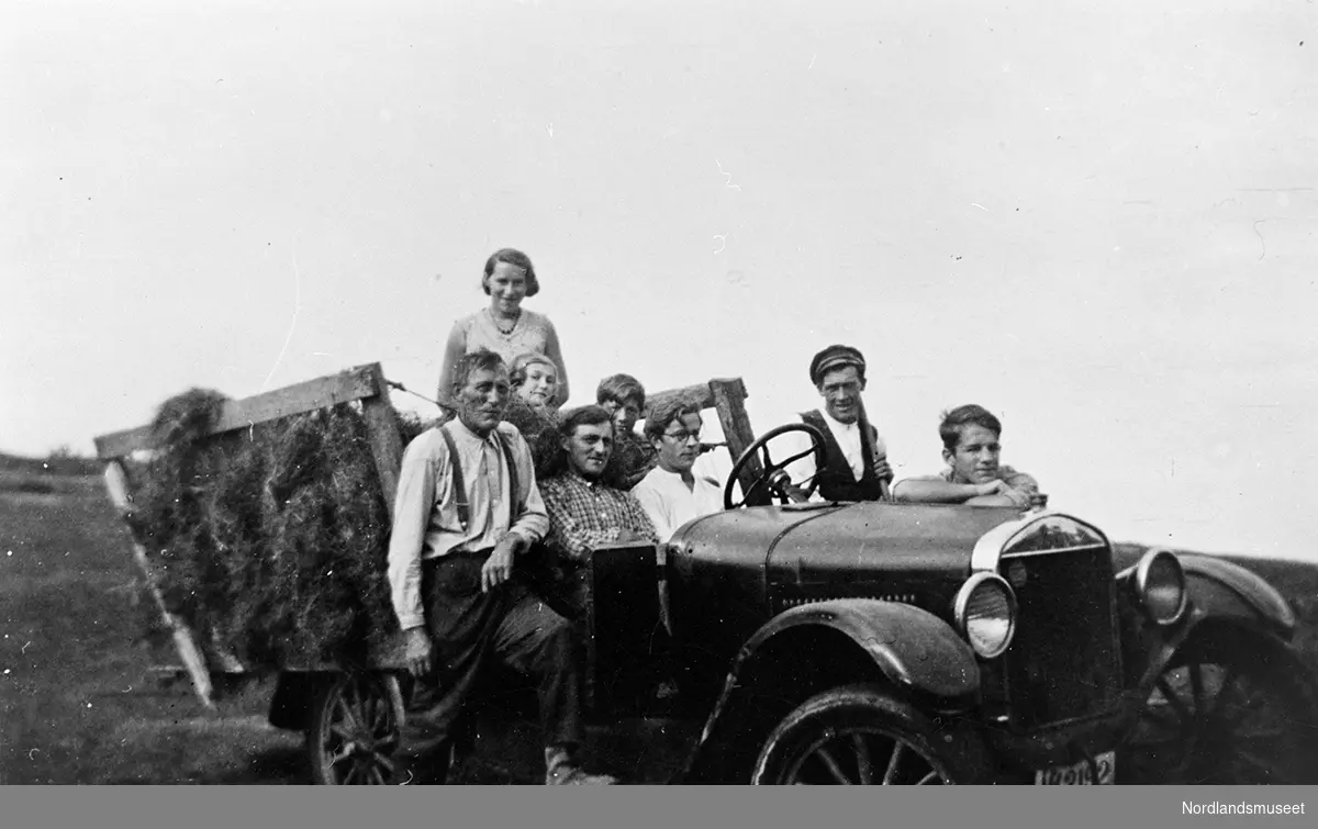 En del mennesker ved og i en bil med høy-last. Bilen er en Ford T 1926-27-modell. Fra venstre foran: Jeremias Hansen og Edgar Jensen. Ved rattet Bjarne Fygle. Normann Hansen står ved bilen. Han som støtter seg på bilen er Bjørn Fygle. Damene i høyvogna er fra venstre: Ragna Nordvoll og Lillemor Fygle.