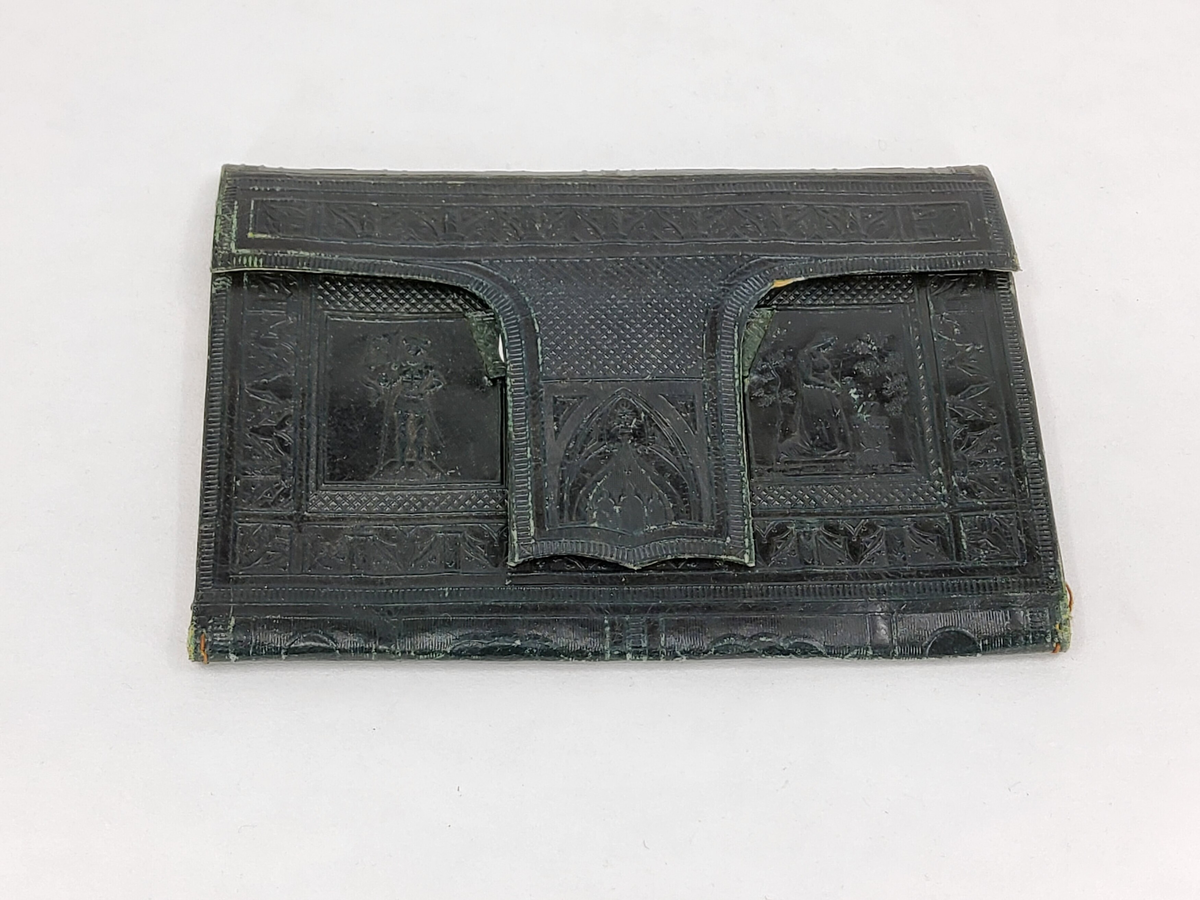 Plånbok av mörkgrönt skinn med pressat mönster på ena sidan föreställande "Luther kastar bläckhornet på den onde". På insidan två fack samt almanacka-anteckningsbok med tryckta mönster i sjvart. Tujnga att trä genom tvärband för låsning. Ej använd.