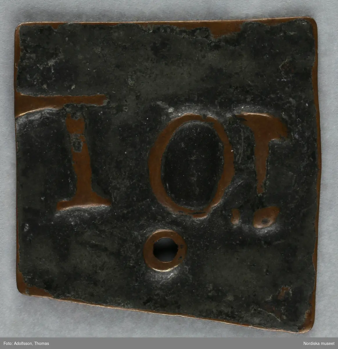 Pollett, av koppar, fyrkantig, ett hål, präglad text: "10 T".