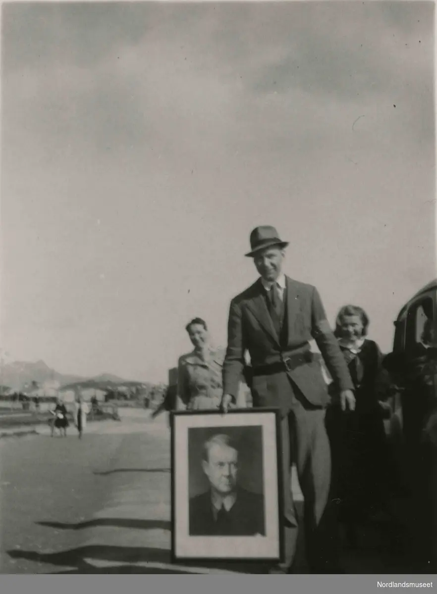 En dresskledt mann holder et bilde av Vidkun Quisling. Bilde tatt i Bodø under feiring av freden etter okkupasjonen 1945.