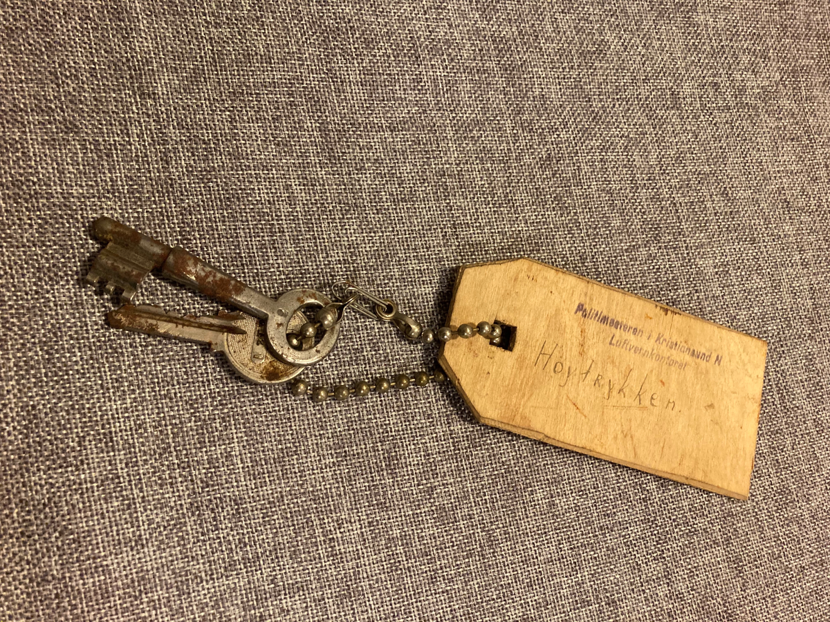 To nøkler holdt sammen i et knippe med et metallkjede. Merkelapp i tre.