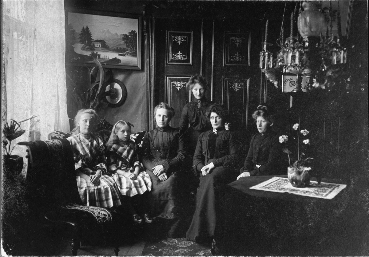 Gruppeportrett av seks kvinner og jenter, fotografert i en stue.