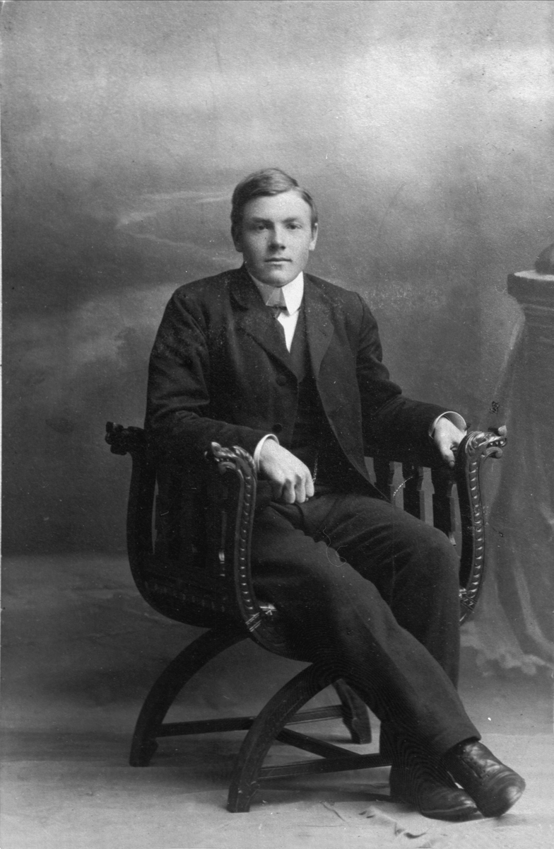 Studioportrett av en ung mann sittende i en stol.