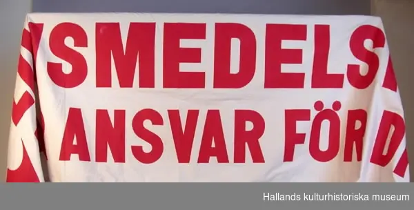 Banderoll av oblekt bomullsväv med röd, målad text: "LIVSMEDELSFACKET TAR ANSVAR FÖR DIN MAT".