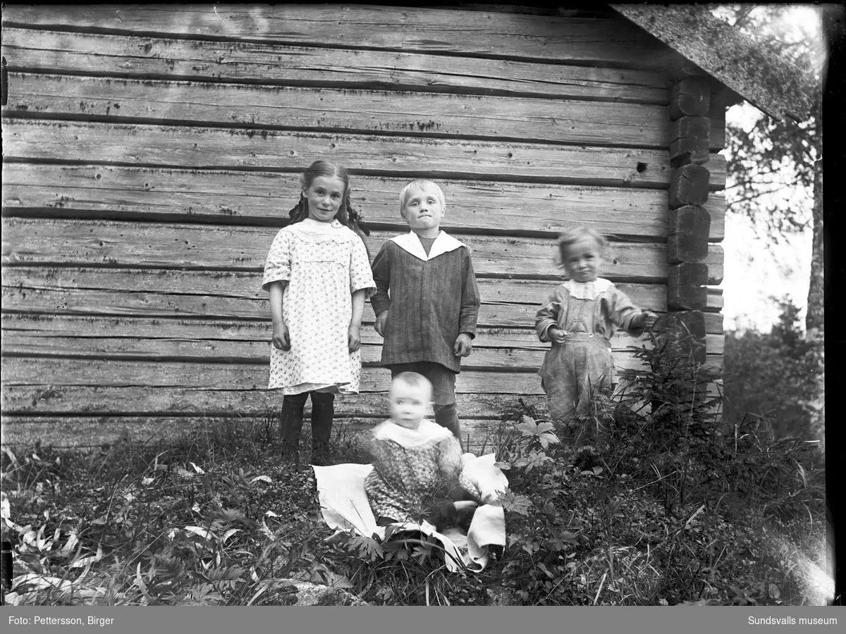 Två familjeporträtt med mor, far och fyra barn invid en liten timrad stuga. På den andra bilden är det enbart syskonskaran.