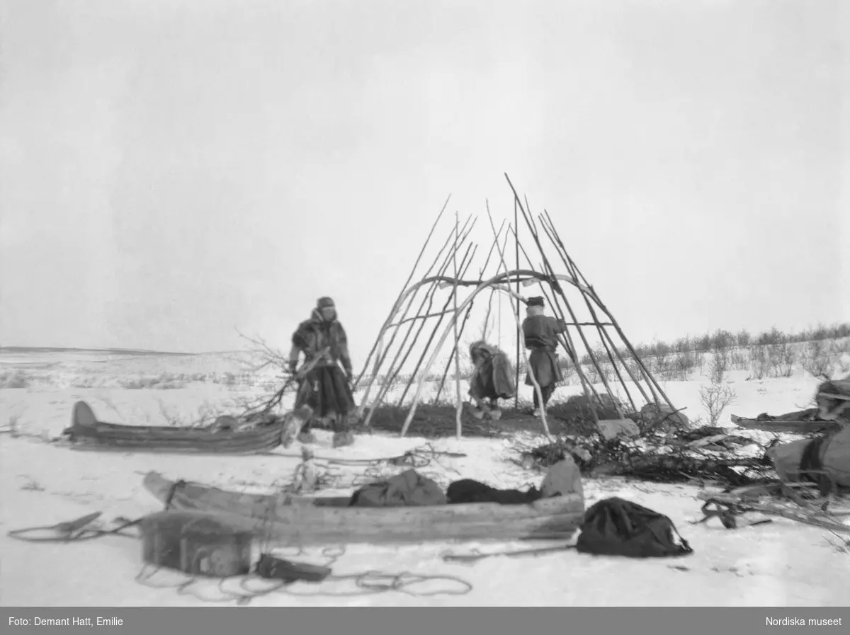 Tre personer, Jouna och Anne Rasti samt deras dotter Marge, har slagit läger och reser en kåta under vårflyttningen från Närvä. Bilden ingår i en serie fotografier tagna av Emilie Demant Hatt i Sapmi mellan åren 1907 och 1916.