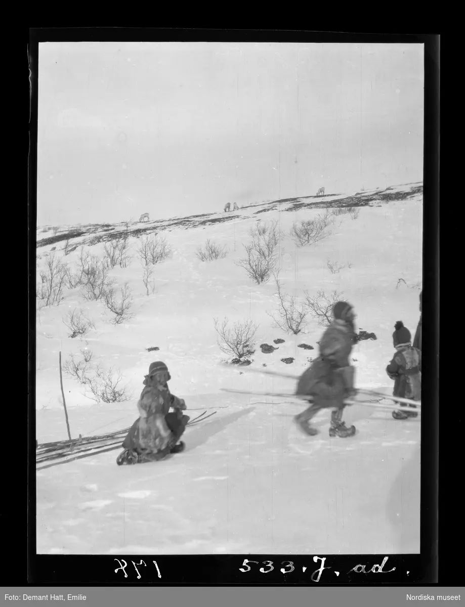 Några barn leker i snön ute i naturen under vårflyttningen från Närvä. Bilden ingår i en serie fotografier tagna av Emilie Demant Hatt i Sapmi mellan åren 1907 och 1916.