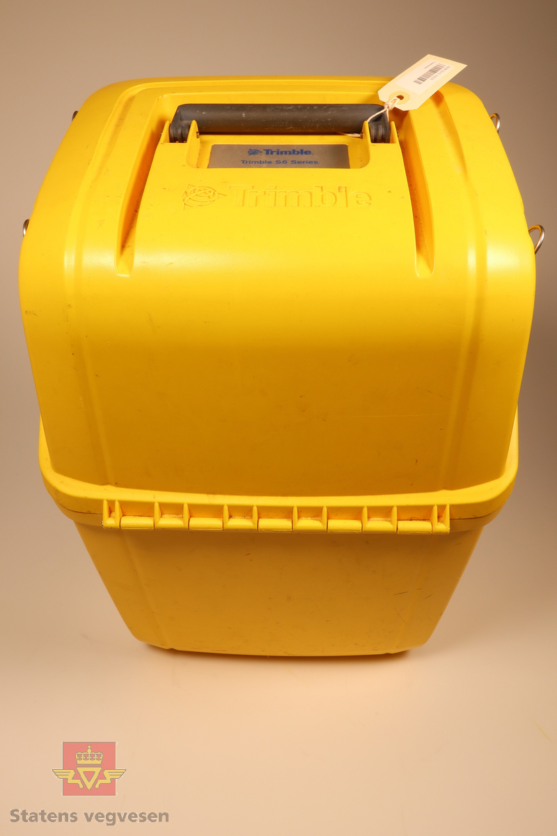 En gul beholder med remmer som inneholder en robot totalstasjon med tilhørende fotplate, adapter, sikteskiver, verktøy, regntrekk, nøkler til beholder, 2stk solblendere, 2stk stylus og en servicerapport.