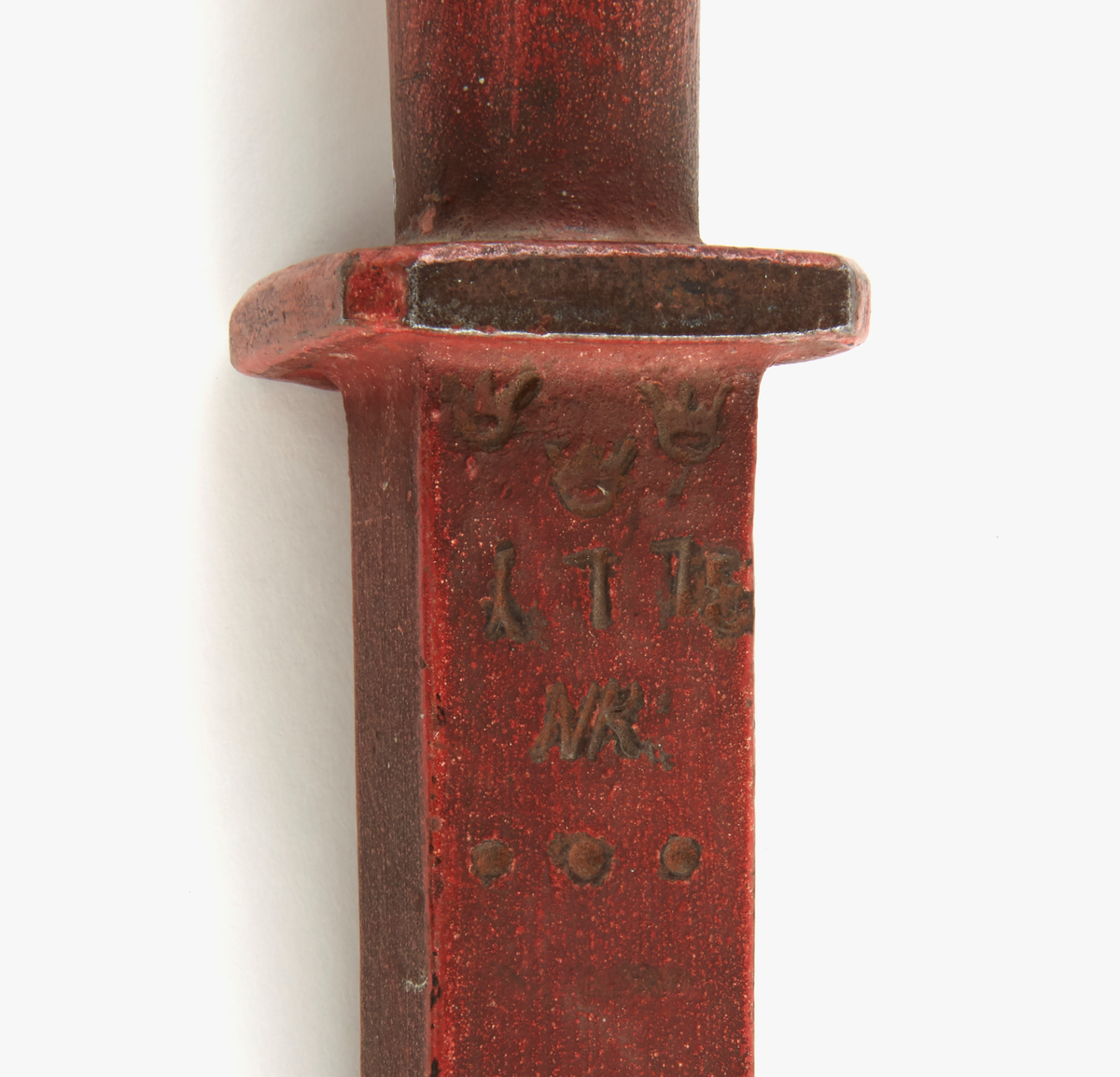 Alnmått av järn, rödmålat. Handtag med ledad ring i ena änden. Krönt med: "tre kronor, 1775, NR".