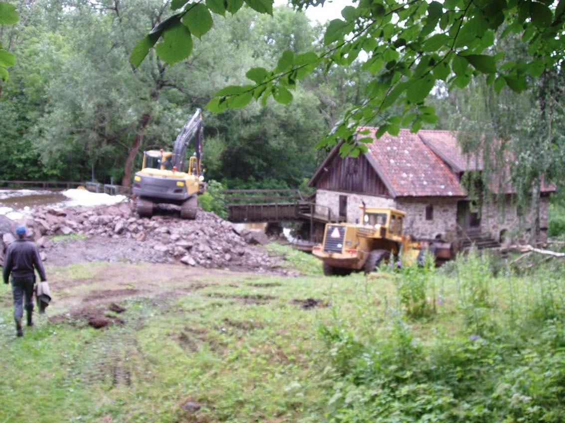 Grävmaskin och hjullastare förstärker dammen vid Rasmus kvarn med sten, i samband med översvämning.