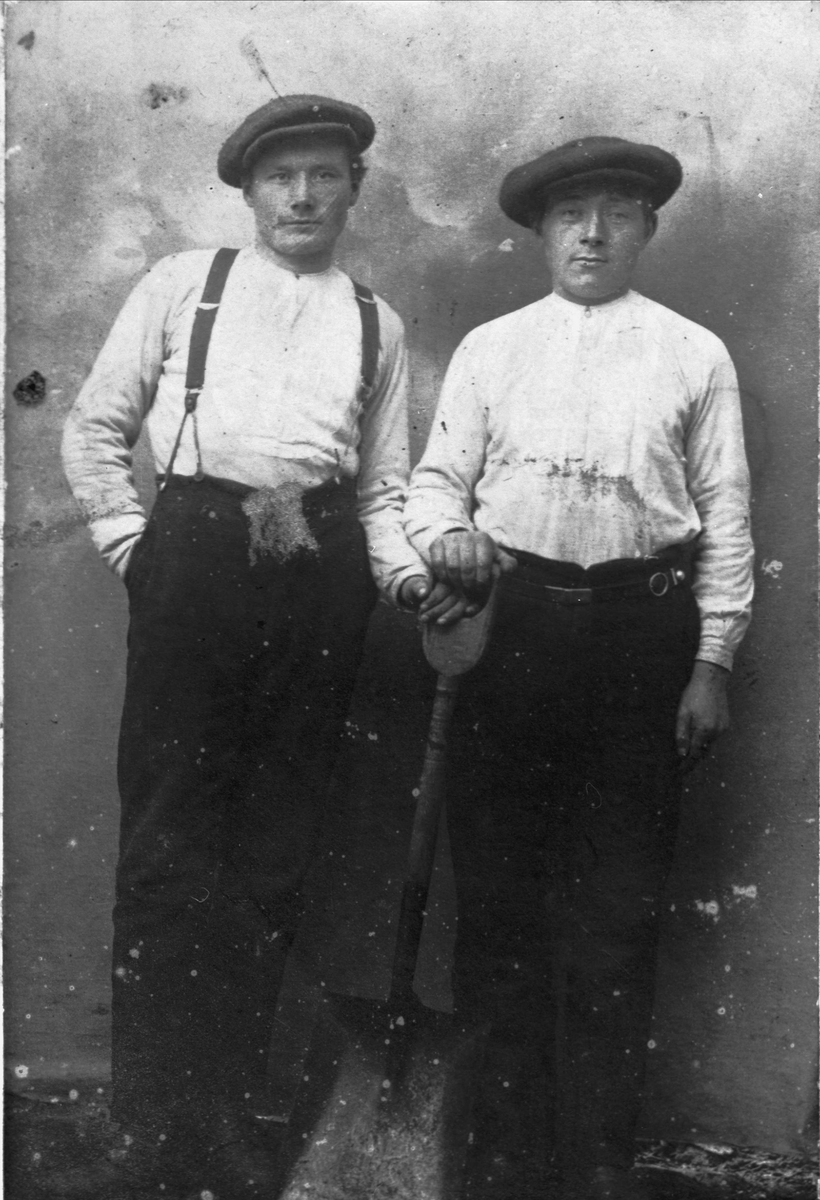 Studioportrett av to brødre, fotografert stående med en spade.