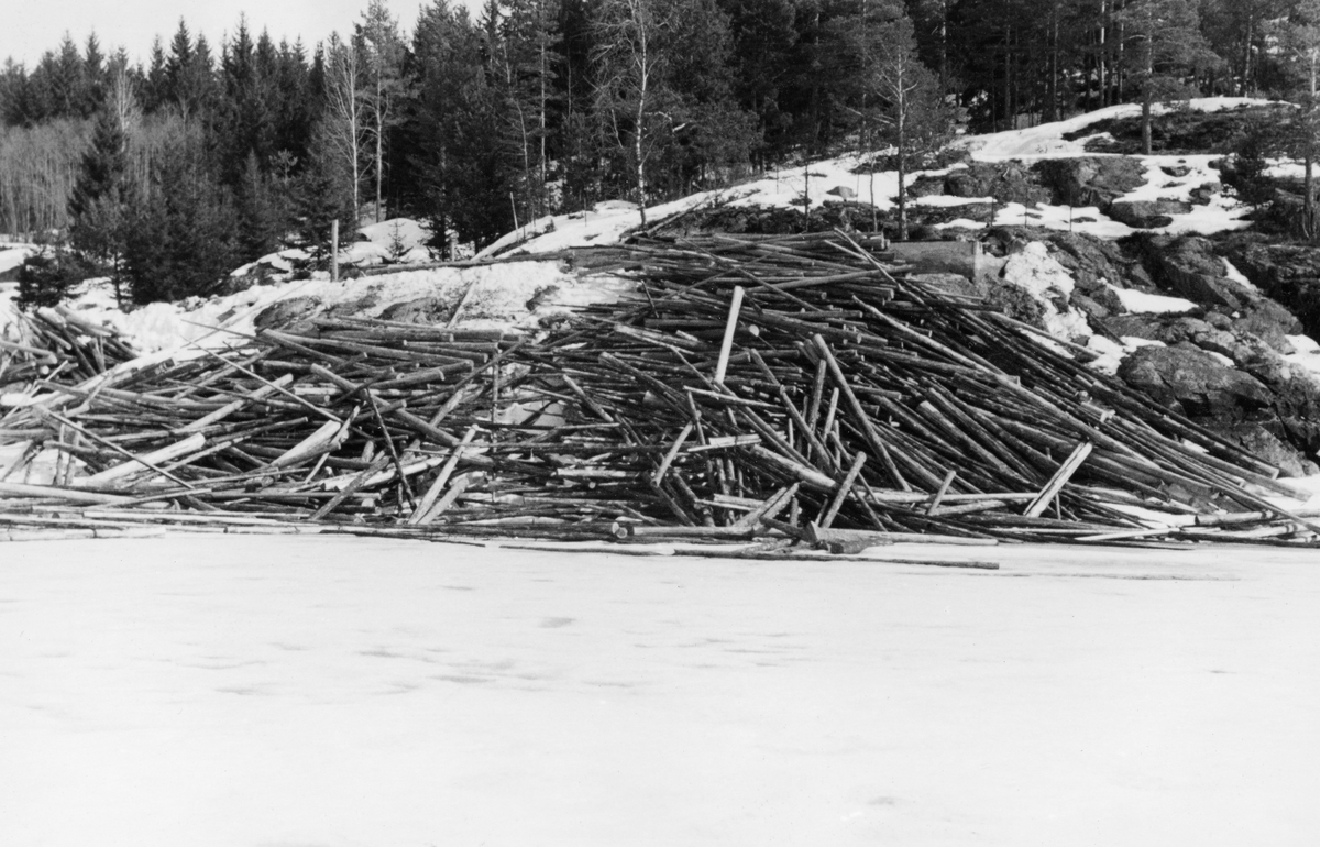 Tømmervelte ved Sæter i Trøgstad kommune i Østfold vinteren 1954.  Fotografiet viser hvordan tømmeret er veltet fra en bergrygg mot den islagte og snødekte flata på innsjøen Øyeren.  Stokkene ligger hulter til bulter, dels i skråningen ned mot vassdraget, dels på isen.  En slik måte å velte fra seg fløtingstømmer på innebar mye besvær for fløterne.  De stokkene som ble liggende på sjøen ville lett drive av gårde når isen gikk, før man rakk å "soppe" (bunte) dem, de som lå hulter til bulter i skråningen ned mot stranda ble det tungt og vanskelig å få på vannet.  Tømmerveltene skulle helst ligge luftig til på strandbrinken, med stokkenes lengderetning parallelt, slik at de lettvint kunne rulles uti når tida var moden for det.  Dette fotografiet ble antakelig tatt for å få leverandøren (i dette tilfellet Borregaard) til å innskjerpe slike rutiner for sine folk. 