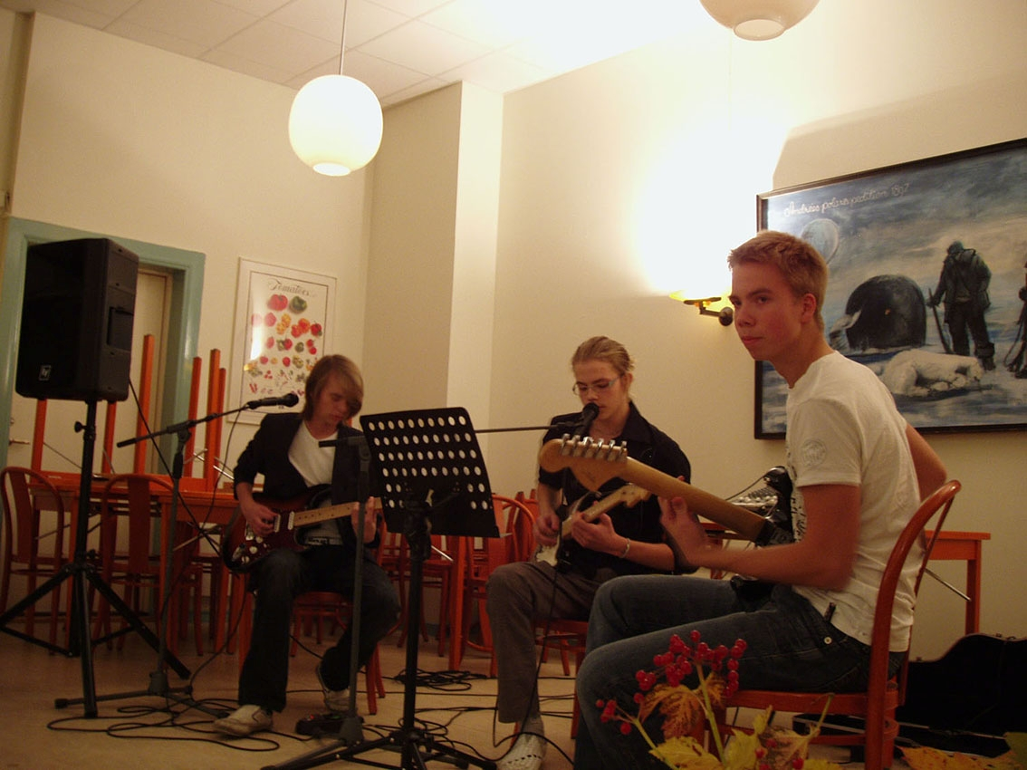 Tre tonåriga pojkar spelar musik på en scen; två gitarrer och en bas.