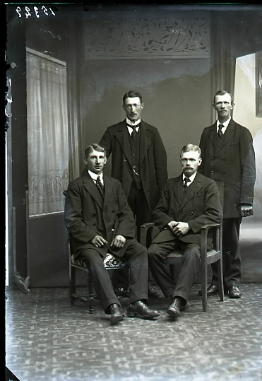 Ateljéfoto av fyra män i helfigur varav två sitter. Beställare och troligen en av männen på bilden är Albin Andrén, Fjärås.