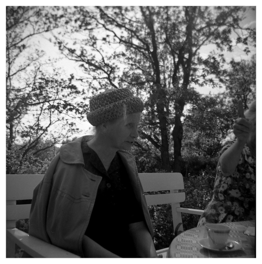I familjen Svanbergs trädgård på Södra Kyrkvägen 10 "Villa Gläntan" 1960-tal. Goda vännen Agnes Ekstedt (1898 - 1984), iklädd kappa och hatt, är på besök. Hon sitter i en träsoffa.
Relaterat motiv: A4514.