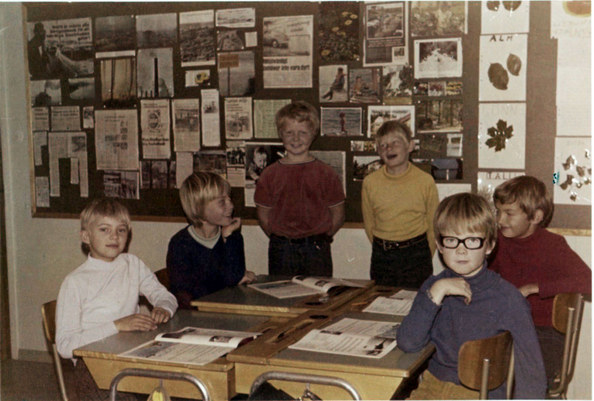 Sex elever (pojkar) befinner sig i en skolsal på Brattåsskolan, 1980-tal. Fyra utav dem sitter vid sina bänkar och två står upp.