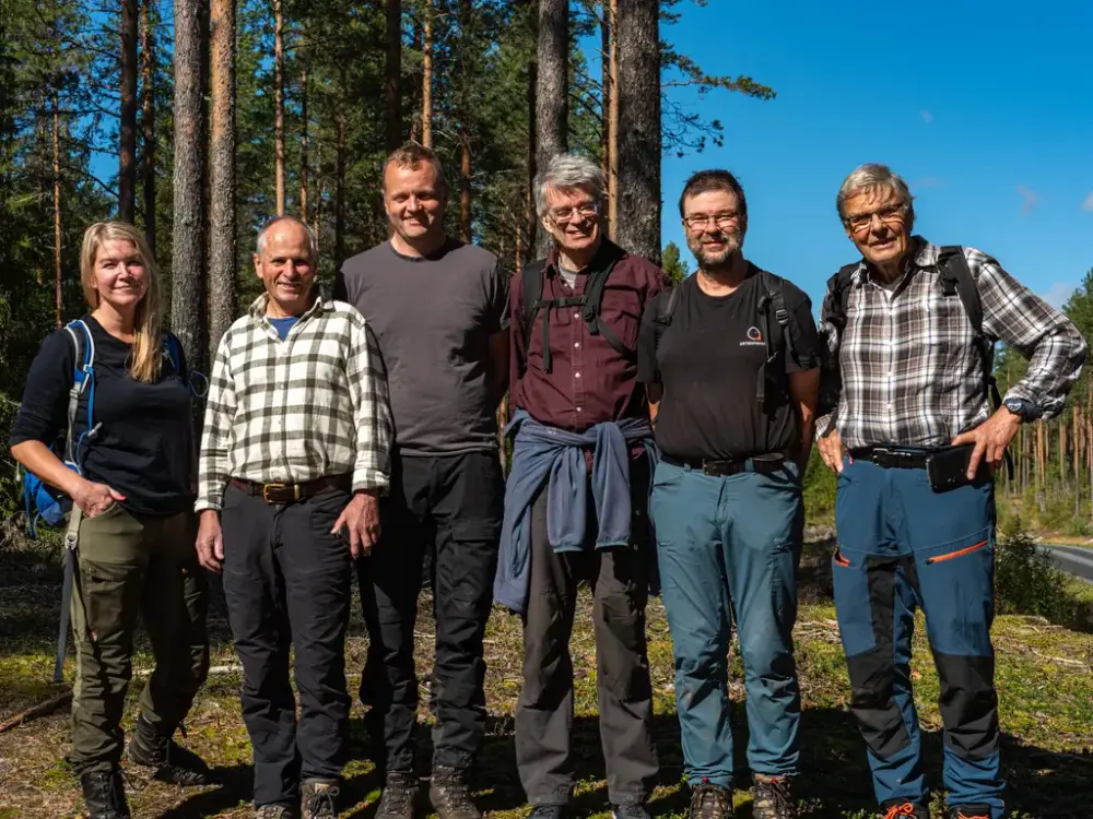 En gruppe mennesker står i skogen. De har på seg turklær. På bildet er det en kvinne og fem menn.