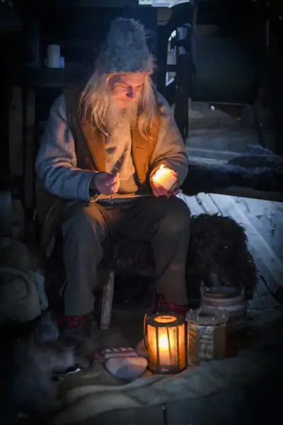 Gråkledd låvenisse med fyrstikk og talglys.