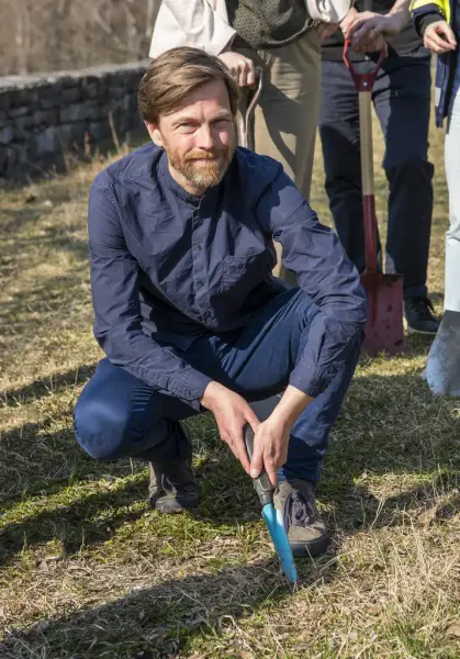 Den danske arkitekten Kristian Langkilde sitter på huk med en liten hagespade.