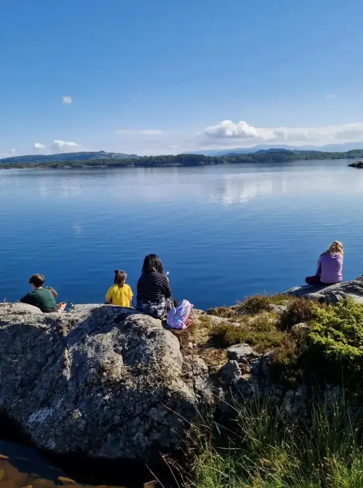 Folk nyter sommerdag ved stille blå fjord og blå lettskyet himmel