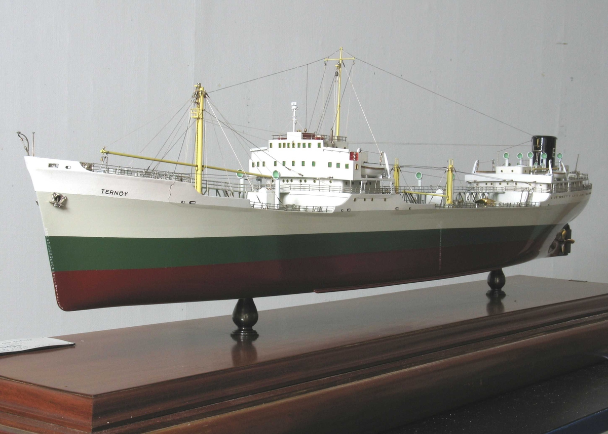 Skipsmodell, profesjonelt utført, montert på mahognyplate i glassmonter. Tankskipet  Ternøy", tilhørende Olaf Boes rederi, Arendal. Skroget malt lysgrått, grønt med rødbrun kjøl. På sort skorstein en hvit B.